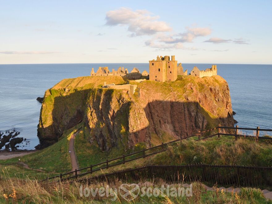 Dunnottar Castle on sea cliffs at sunset seen from the entry path