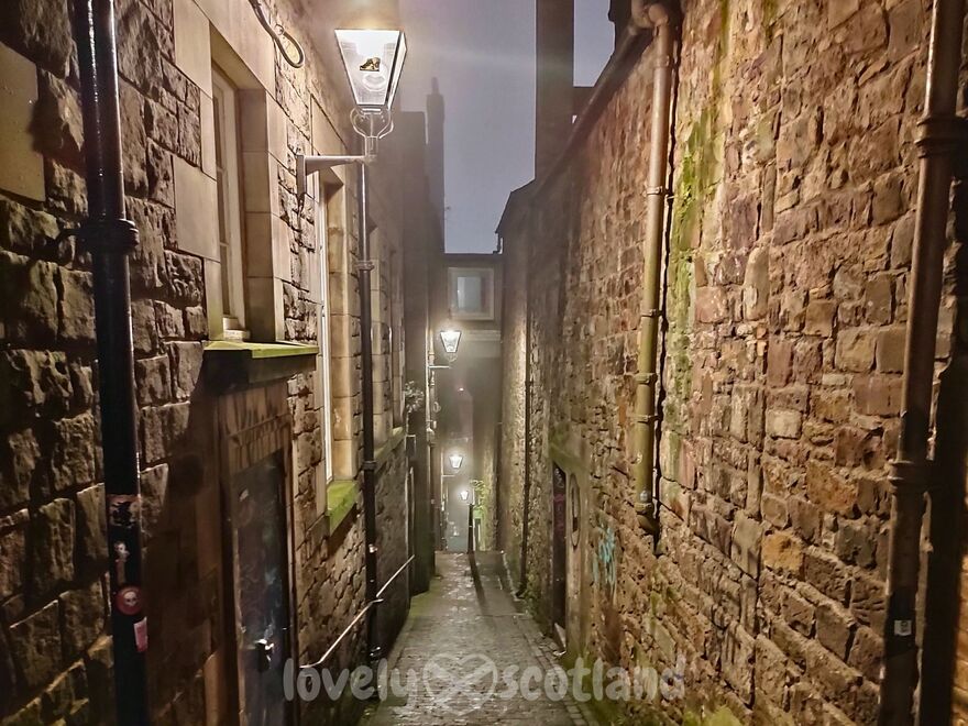 Anchor Close en Edimburgo de noche con niebla muros de piedra y faroles