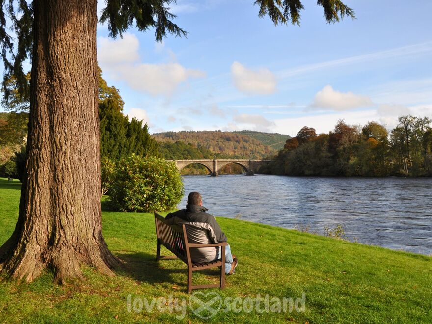 Hombre sentado en un banco junto al río Tay en Dunkeld en un día soleado