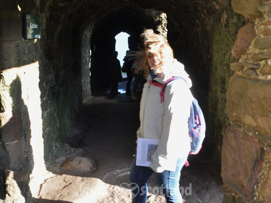 Traveler inside Dunnottar Castle with windblown hair in a dark stone passage