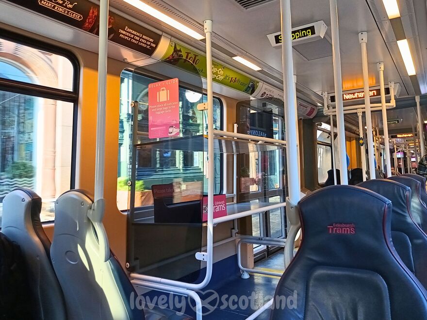 Interior of an Edinburgh tram with seats luggage area and next stop display