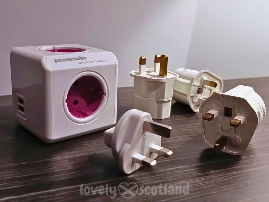 Several UK Type G adapters and a PowerCube travel power strip on a table